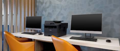 Un espacio de trabajo con dos monitores, una impresora y dos sillas naranjas.