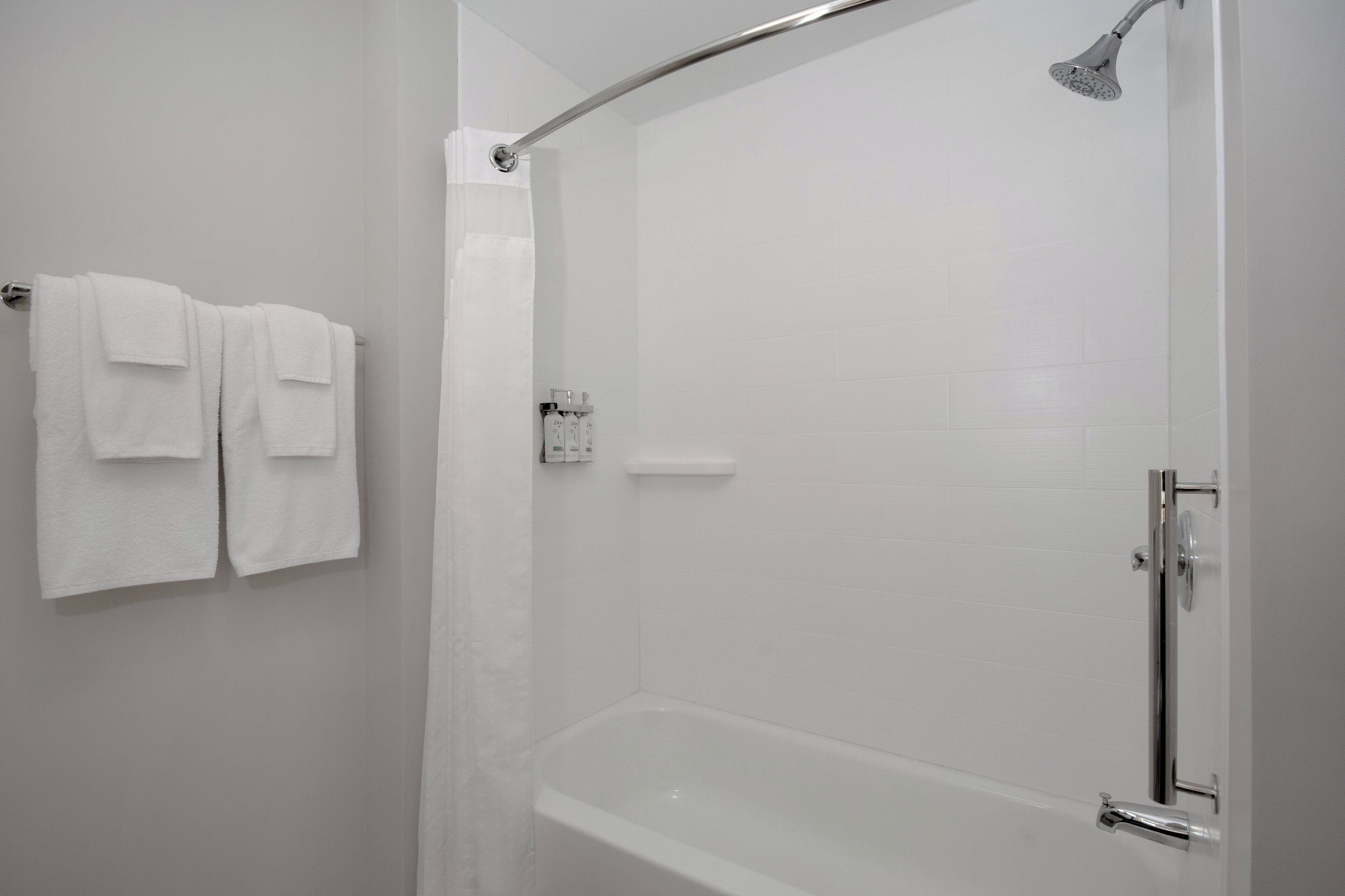 Un baño con ducha, bañera y un perchero con dos toallas.