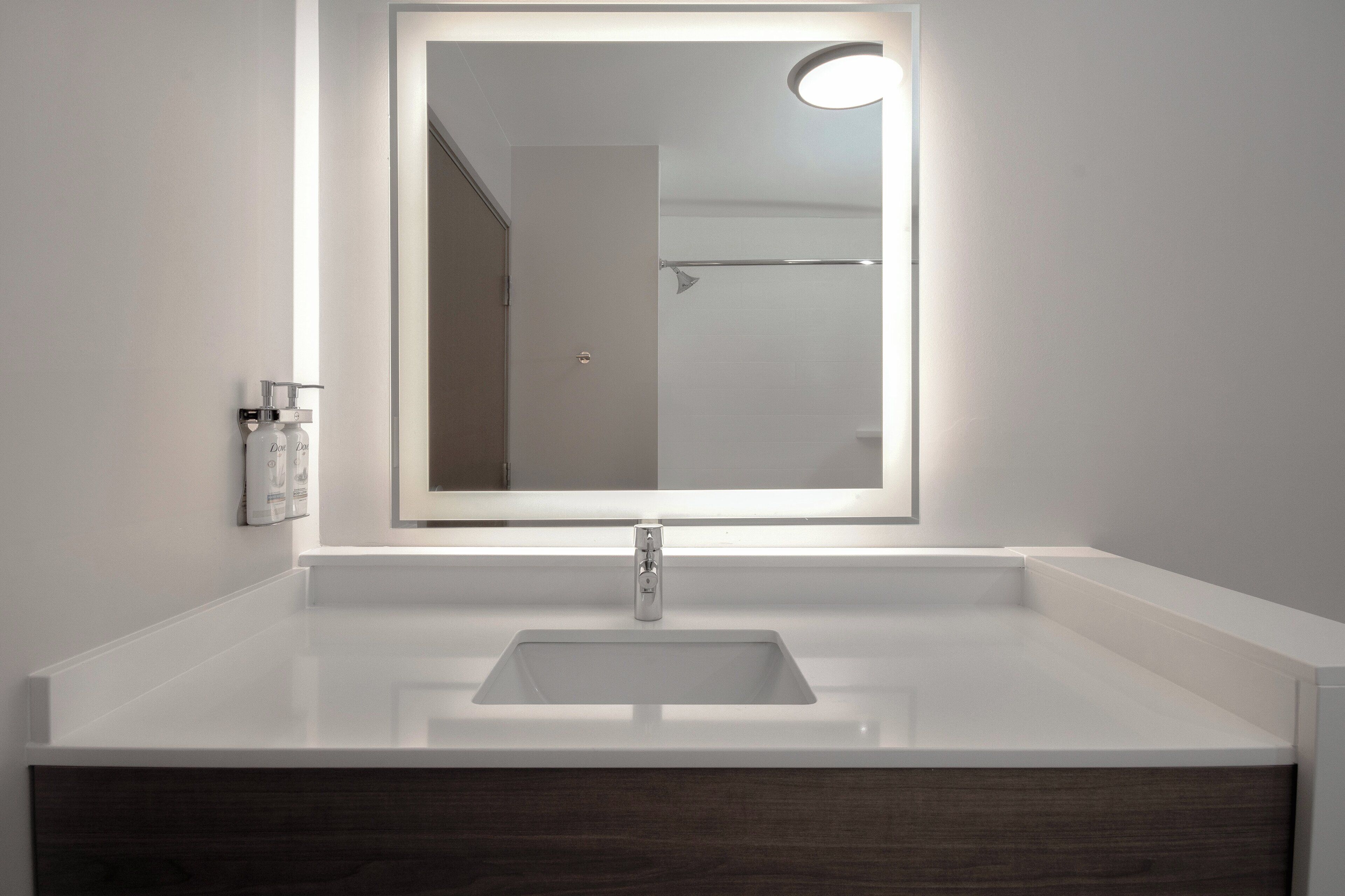 A bathroom with a white sink, a mirror with a light, and a door in the background.