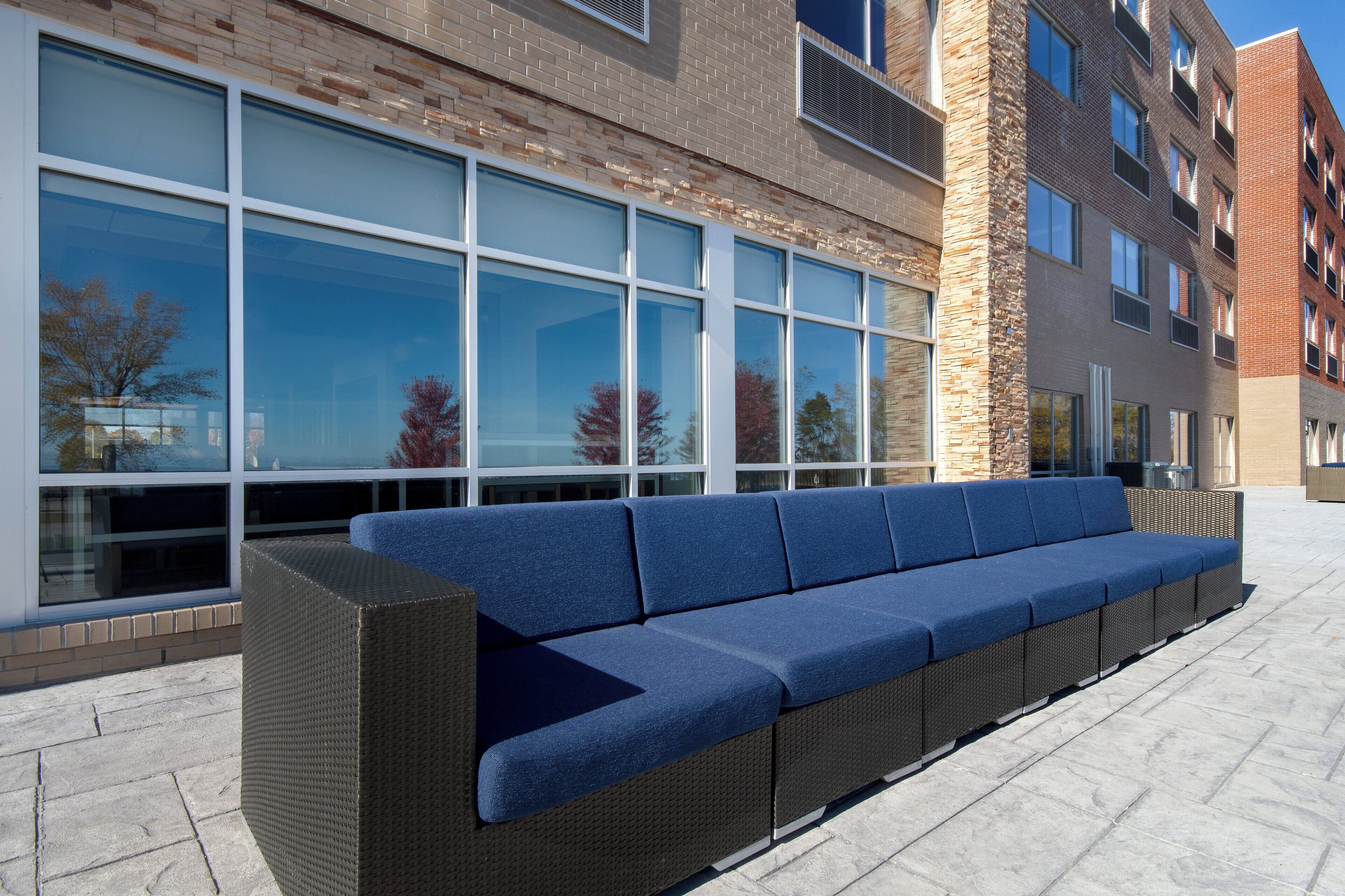 A long, blue cushioned bench outside a building with large windows and a stone facade.