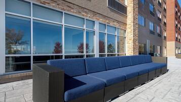 A long, blue cushioned bench outside a building with large windows and a stone facade.