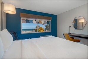 A hotel room with a large bed, a view of the beach, a window with a view of the sea, a chair, and a desk with a lamp. - Holiday Inn Express and Suites Oscoda by IHG (Oscoda)