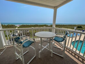 A covered outdoor area with a table and chairs, a view of the beach and ocean, and a pool. - 2BR OF condo. Walk-up. Pool. Perfect getaway in Windy Hill. (North Myrtle Beach)
