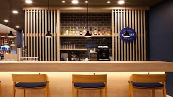 Un espace bar comprenant un comptoir, des tabourets de bar et un mur où sont exposées des bouteilles.