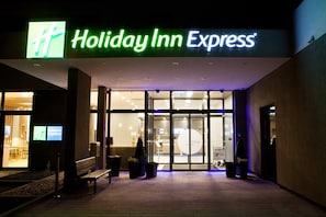 The exterior of a Holiday Inn Express hotel with a glass entrance and a bench outside. - Holiday Inn Express Bochum by IHG (Bochum)