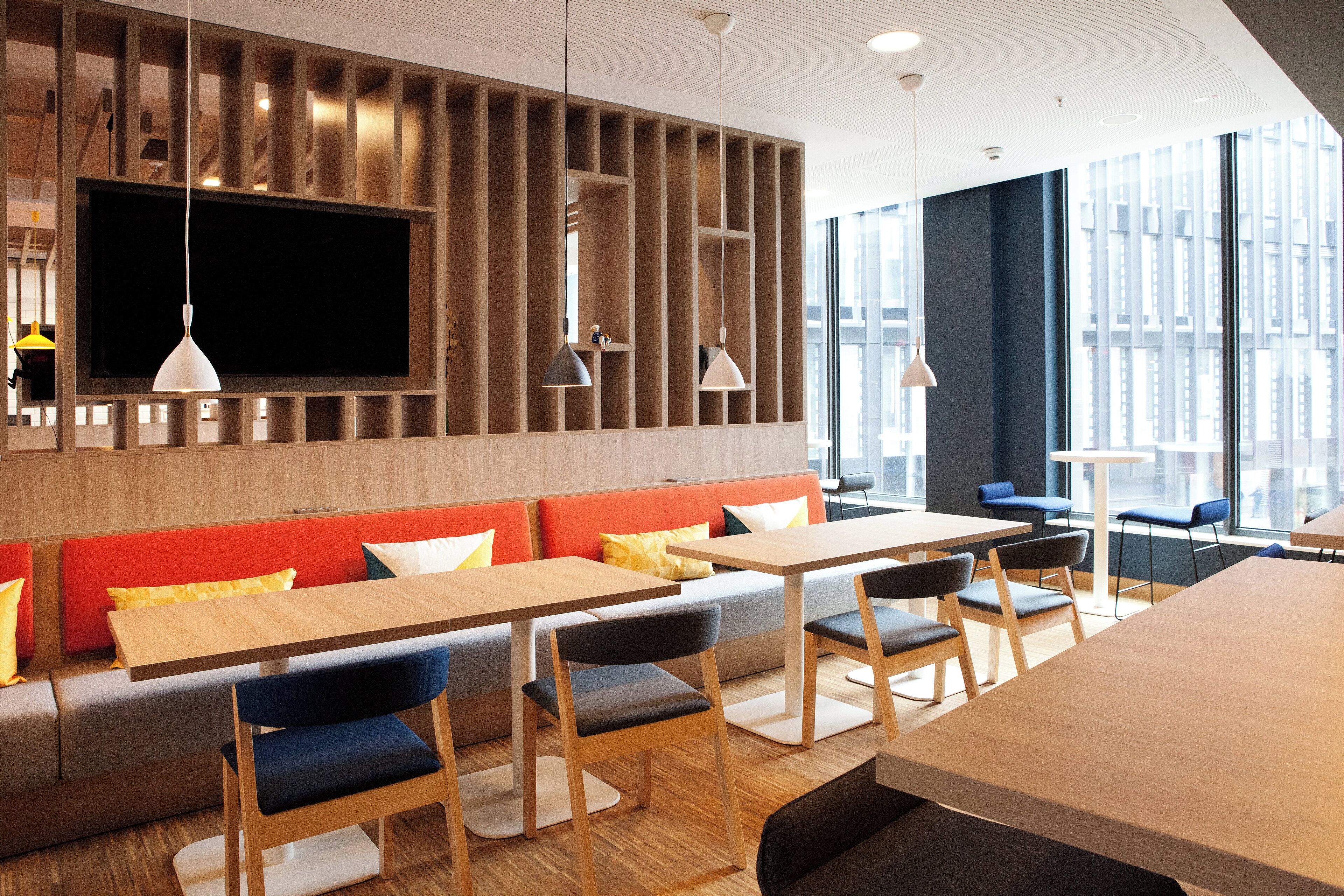 A modern dining area with wooden tables and benches, a large flat-screen TV, and pendant lighting.