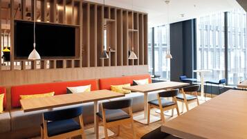 A modern dining area with wooden tables and benches, a large flat-screen TV, and pendant lighting.