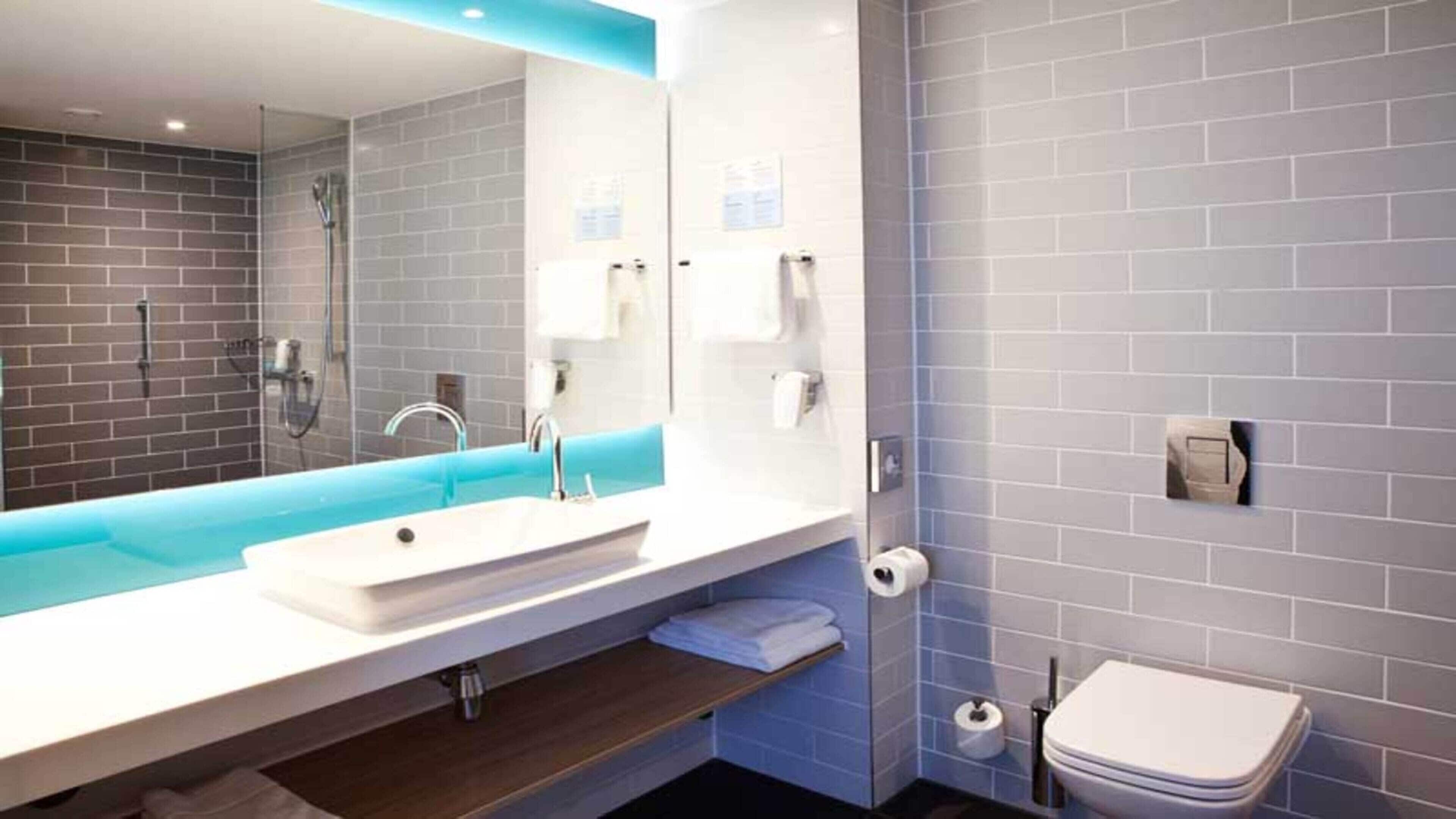 A modern bathroom with a large mirror, a sink, a shower, and a toilet.