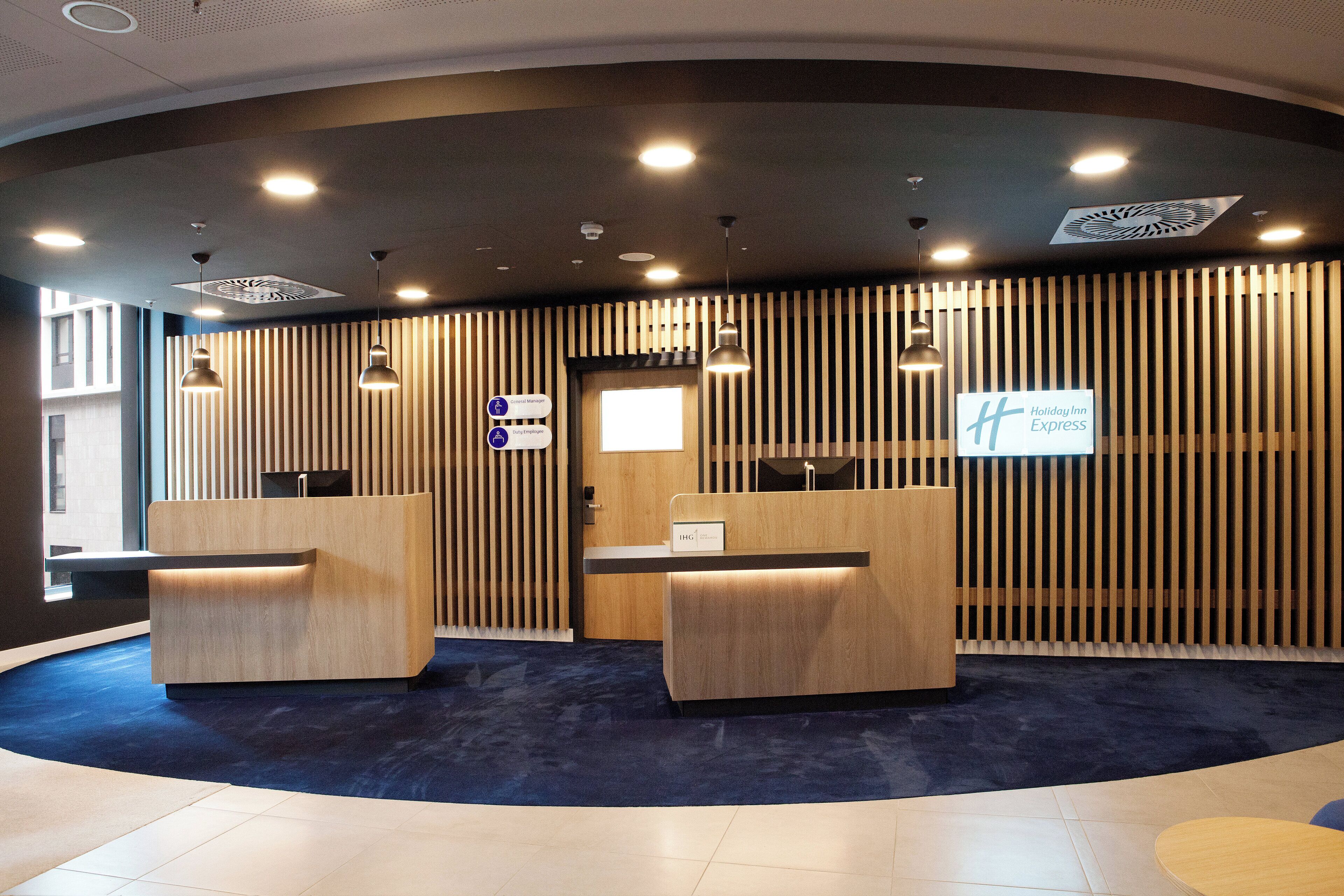 A reception area with two wooden reception desks, a blue carpeted floor, and a sign for Holiday Inn Express.