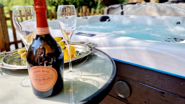 A hot tub with a glass table in front, a bottle of wine, and two glasses. - 8 Coach House (Preston)