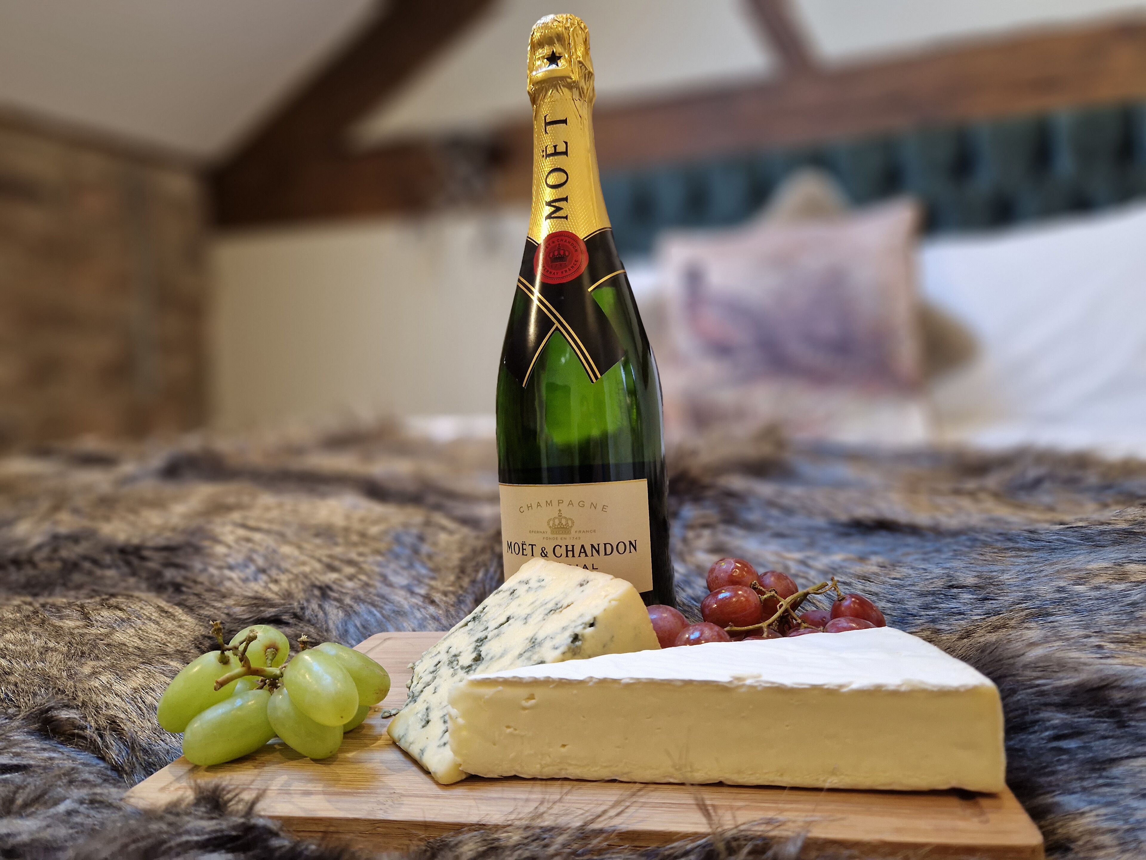 Una botella de champán Moët, queso azul y uvas sobre una tabla de madera en una habitación con decoración rústica.