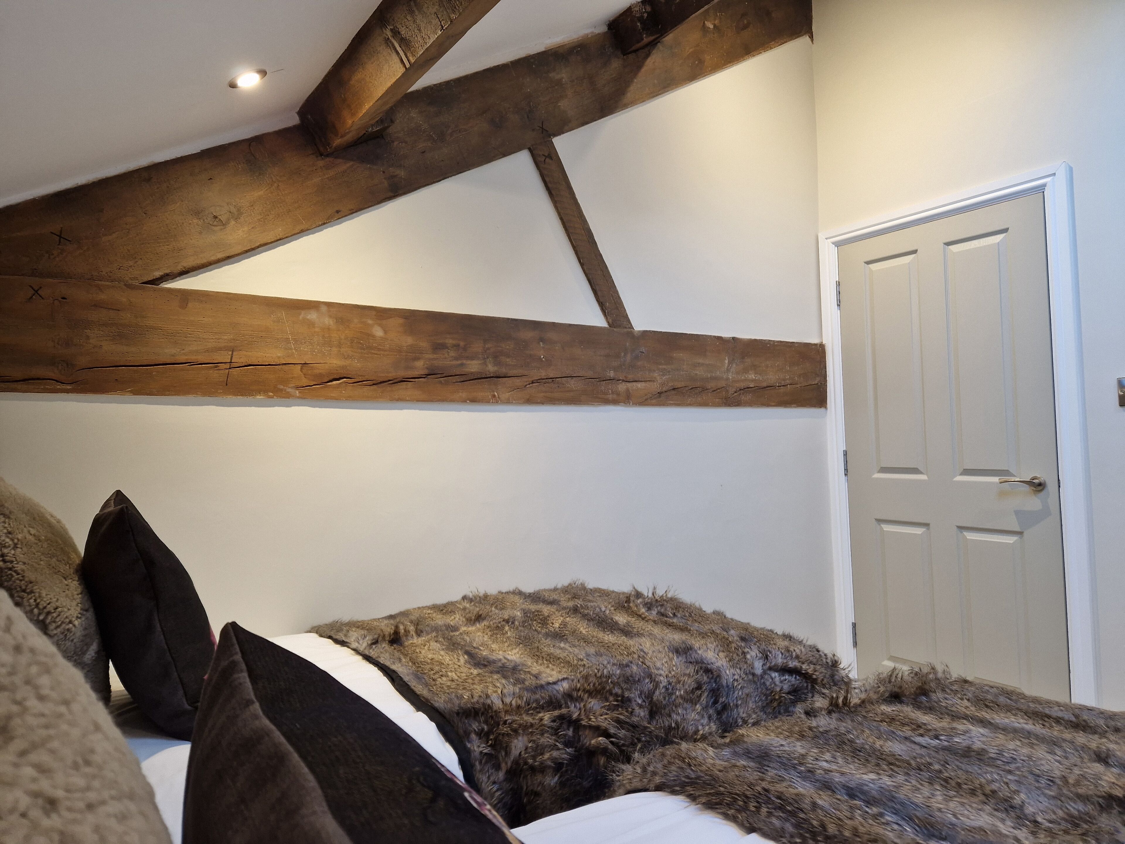 A bedroom with exposed wooden beams, a white door, and a bed with a fur throw.