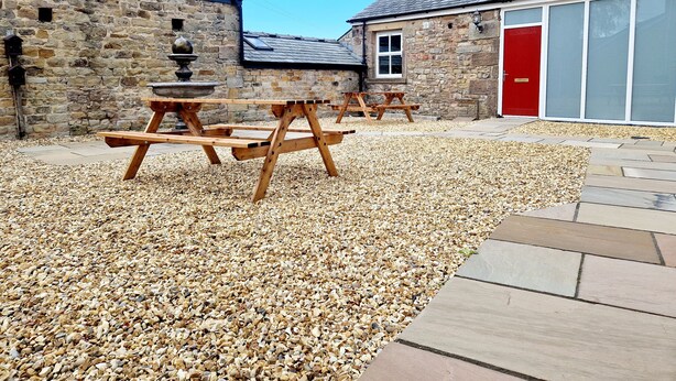 A courtyard with stone buildings, a red door, and wooden picnic tables. - 7 Holly Barn (Preston)
