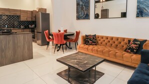 A modern kitchen with a central island, dining area with red chairs, a brown sofa with floral cushions, and a marble coffee table. - 7 Holly Barn (Preston)
