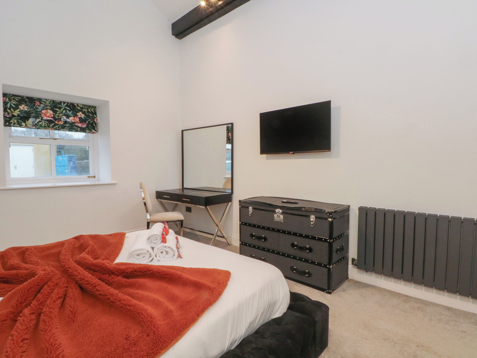 A bedroom with a bed, a dresser, a mirror, a television, and a window with a view of the outside.