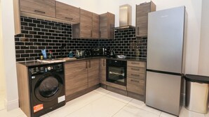A modern kitchen with wooden cabinets, a stainless steel refrigerator, a washing machine, and a tiled backsplash. - 7 Holly Barn (Preston)