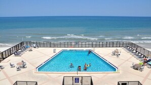 A rooftop pool with a view of the ocean, surrounded by lounge chairs and umbrellas. - Stunning direct ocean front 2 bedroom unit! Fully equipped and all remodeled! (New Smyrna Beach)