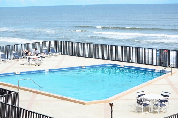 A pool with a view of the ocean, surrounded by lounge chairs and a railing.