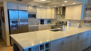 A modern kitchen with a large island, stainless steel appliances, and a tiled backsplash. - Stunning direct ocean front 2 bedroom unit! Fully equipped and all remodeled! (New Smyrna Beach)