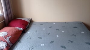Una cama con colcha gris estampada con flores y almohada roja con diseño floral.