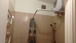 Un espacio de ducha con pared de azulejos, un cabezal de ducha manual y un grifo instalado en la pared.