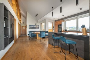 A modern kitchen with wooden beams, a bar area with stools, and a dining area with a table and chairs. - AlpenParks Hotel & Apartment Carpe Solem (Mariapfarr)