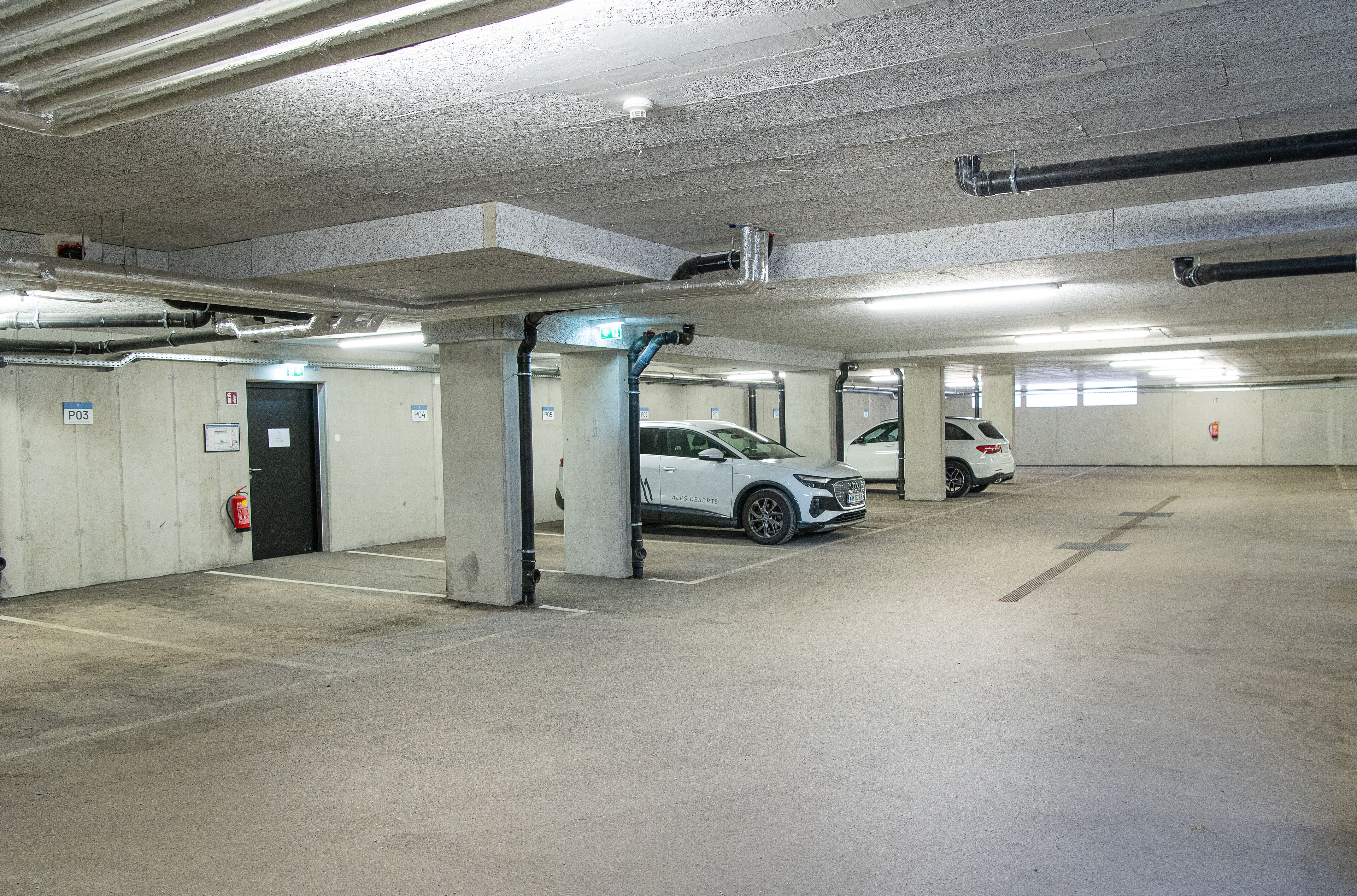 A multi-level parking garage with concrete pillars, emergency exit signs, and fire extinguishers.