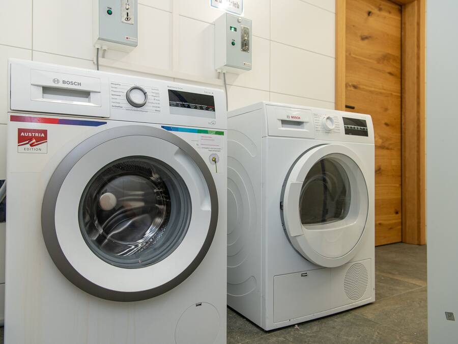 Two Bosch washing machines in a room with tiled walls and a wooden door.