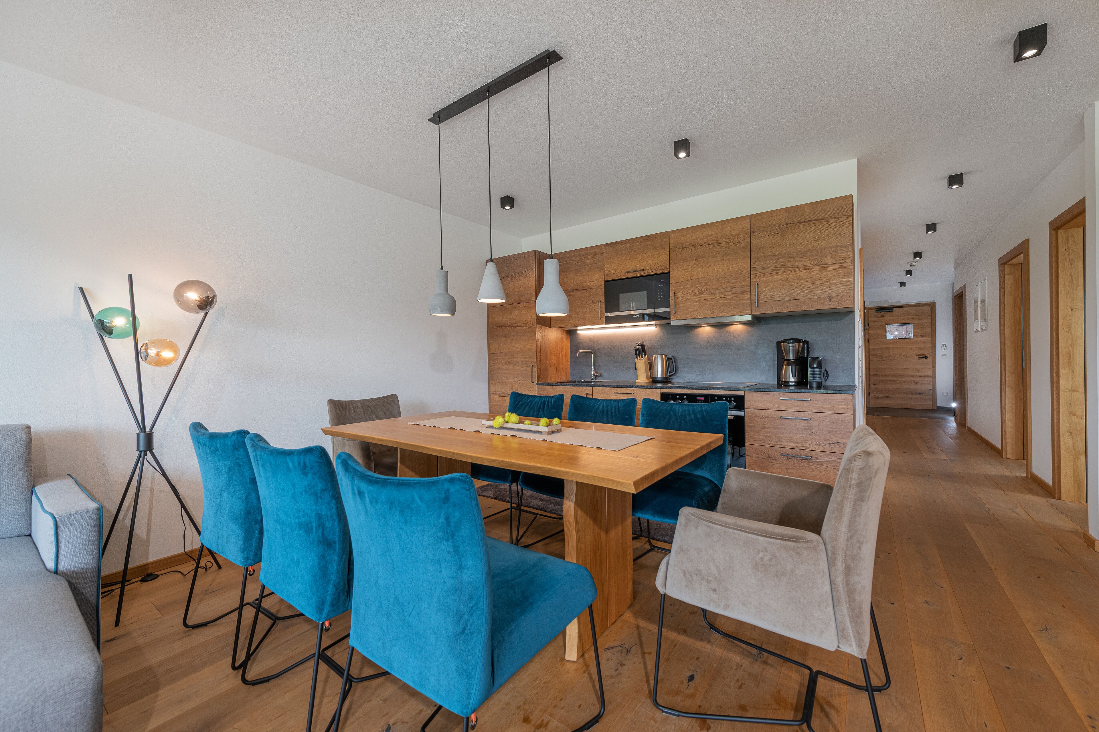 A modern kitchen with wooden cabinets, a central island, and a dining area with blue chairs.