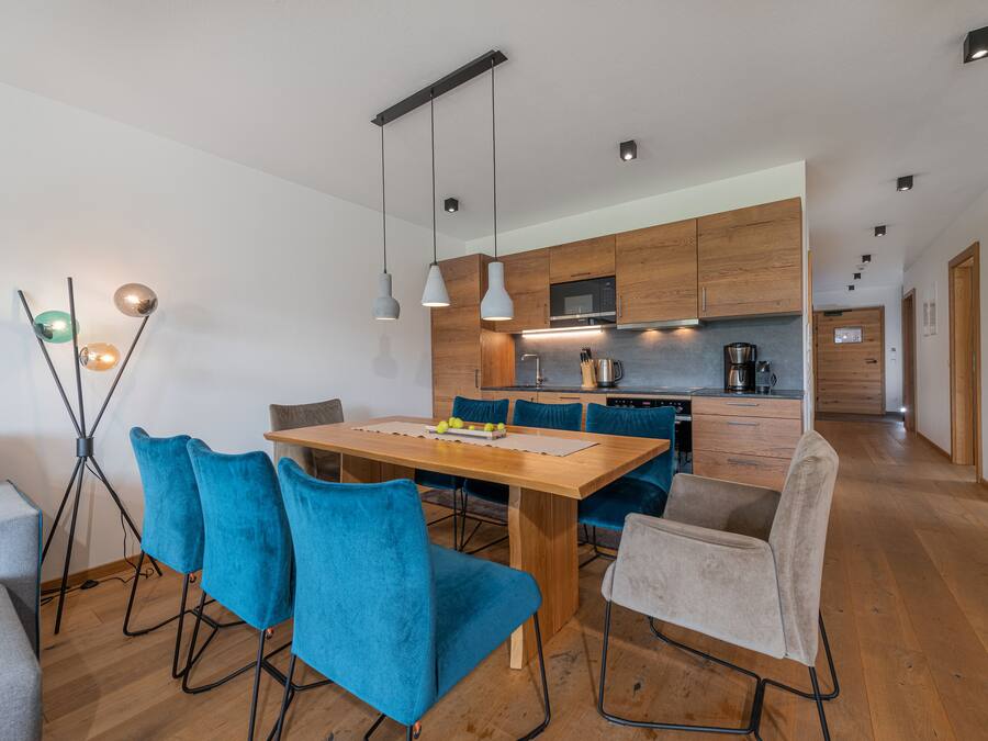 A modern kitchen with wooden cabinets, a central island, and a dining area with blue chairs.