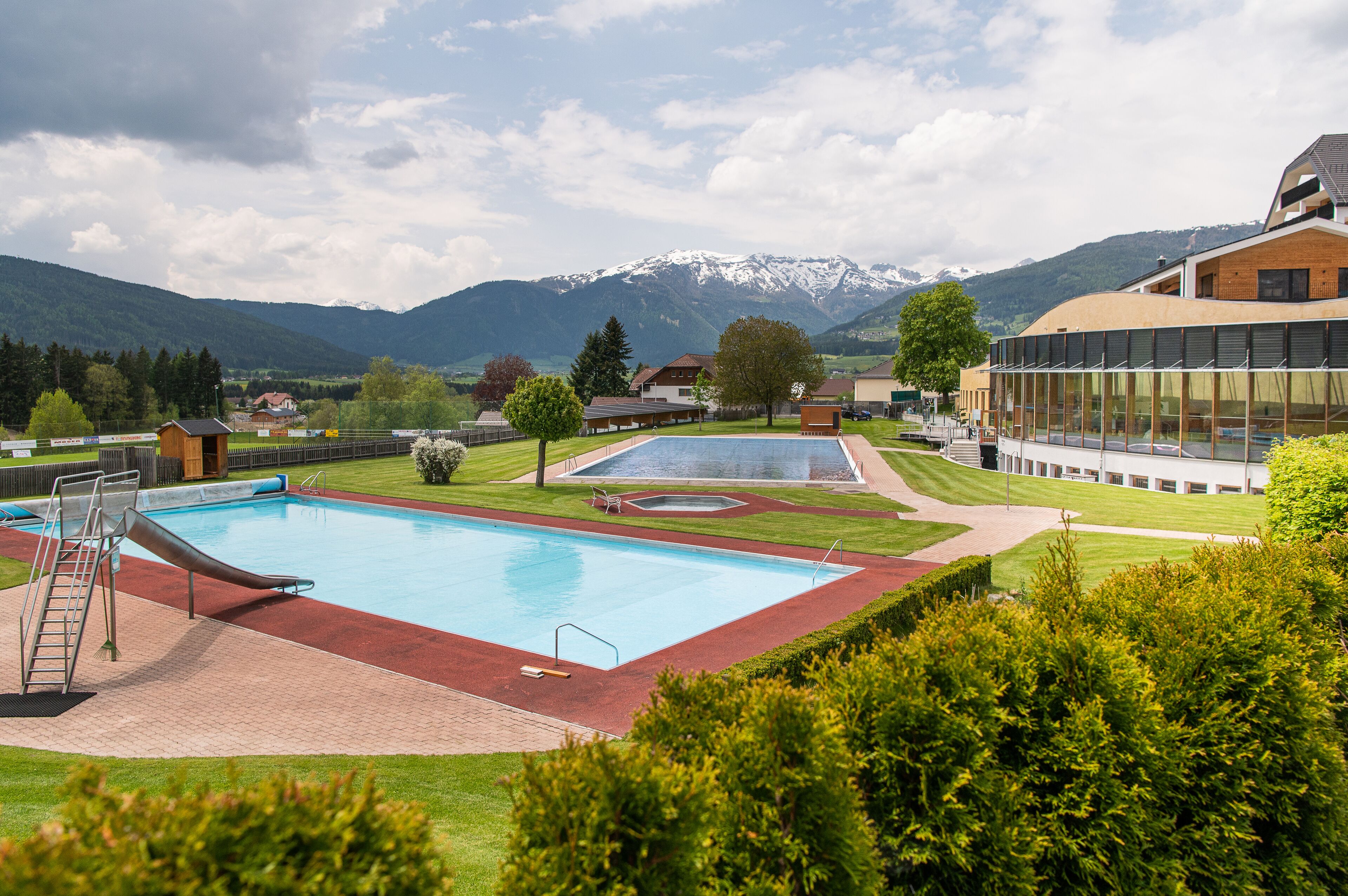 Ein Pool mit Rutsche, umgeben von gepflegten Rasenflächen und einer Bergkulisse.