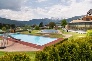 Una piscina con tobogán, rodeada de céspedes cuidados y un paisaje montañoso.