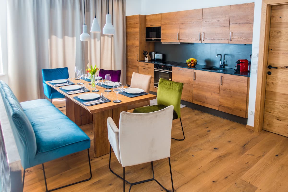 Una cocina moderna con armarios de madera, un comedor con una mesa de madera dispuesta para cuatro personas y un sofá azul.
