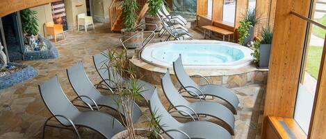 A spacious indoor area with a hot tub, lounge chairs, and potted plants.