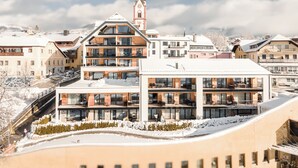 A modern hotel with multiple floors, large windows, and a prominent church spire in the background. - AlpenParks Hotel & Apartment Carpe Solem (Mariapfarr)