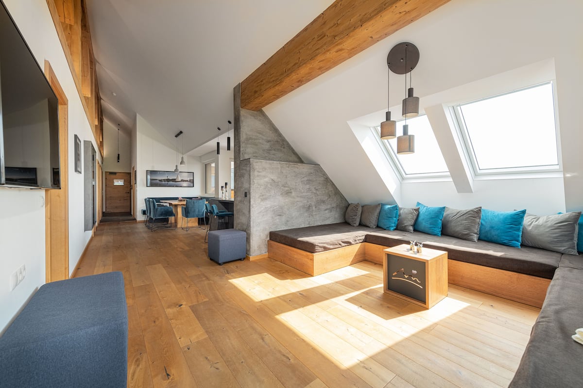Un loft moderno con techo inclinado, vigas de madera, zona de estar integrada, comedor y cocina.