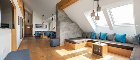 A modern loft apartment with a sloped ceiling, wooden beams, a built-in seating area, a dining space, and a kitchen.
