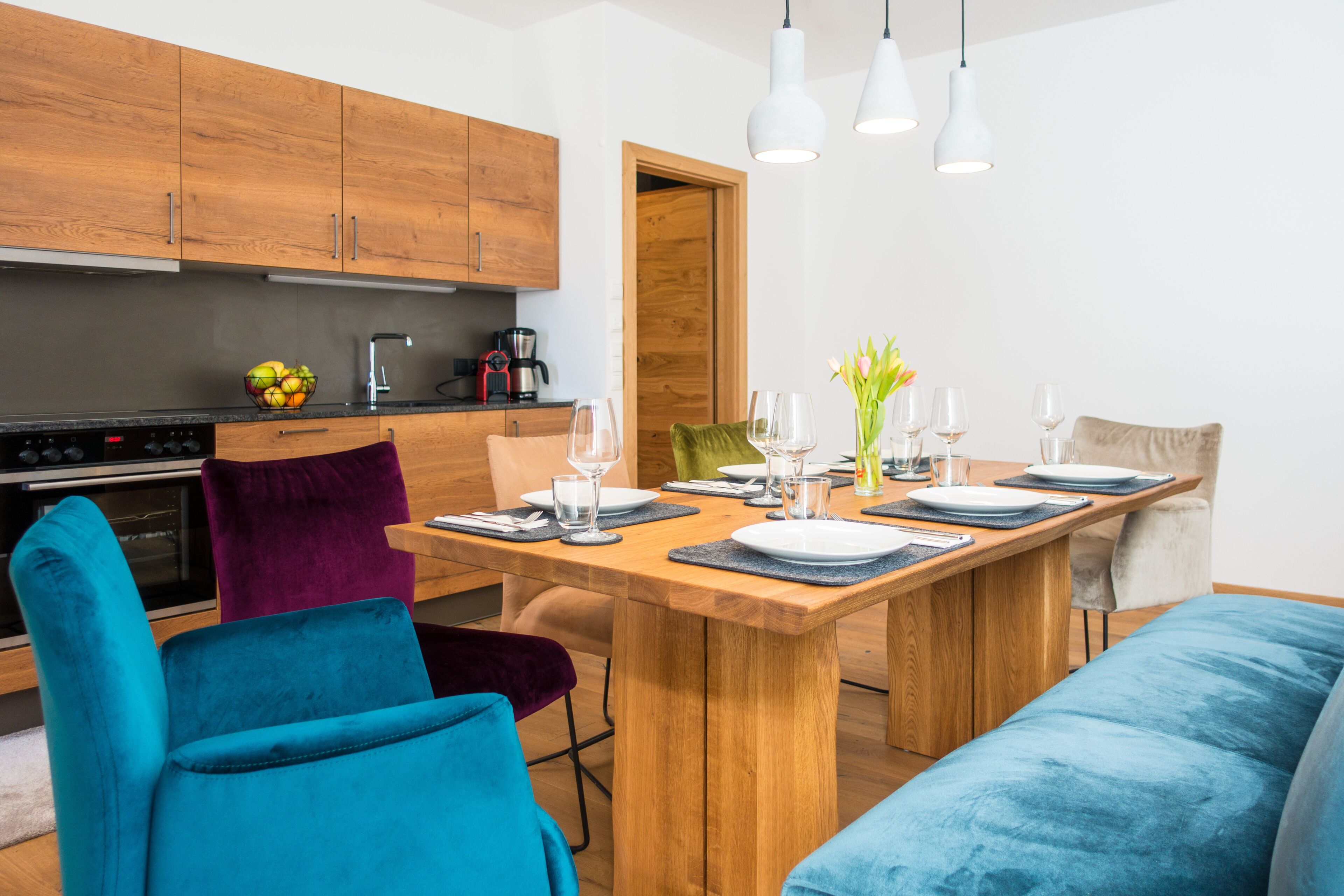 A modern kitchen with wooden cabinets, a dining table set with plates, glasses, and a vase of flowers.