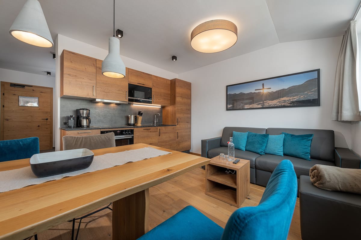 Una cocina moderna con armarios de madera, una mesa de comedor con un tazón y un sofá gris con cojines azules.