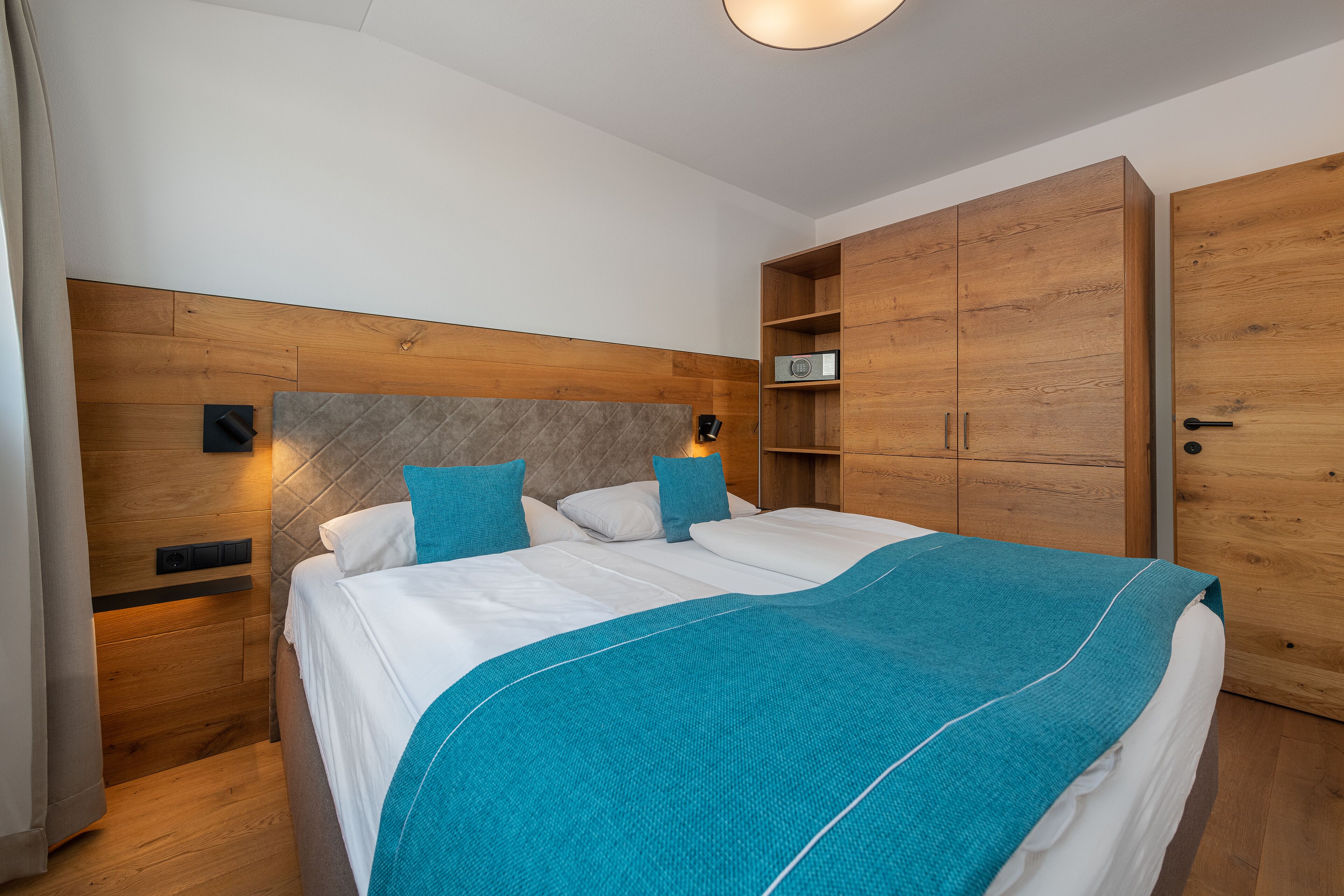 A bedroom with a bed, wooden headboard, nightstands, and a wardrobe.