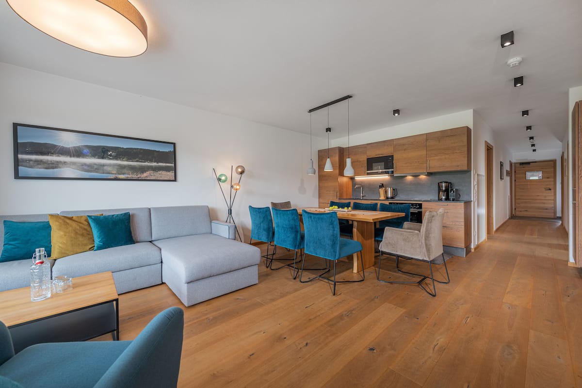 Una sala de estar moderna con sofá, una mesa de comedor con sillas, una cocina con armarios de madera y un pasillo que lleva a otra habitación.