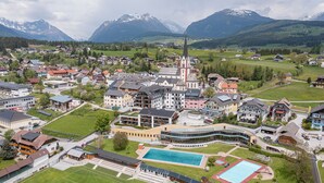 A town with a prominent church, a swimming pool, and a large building with a curved facade. - AlpenParks Hotel & Apartment Carpe Solem (Mariapfarr)