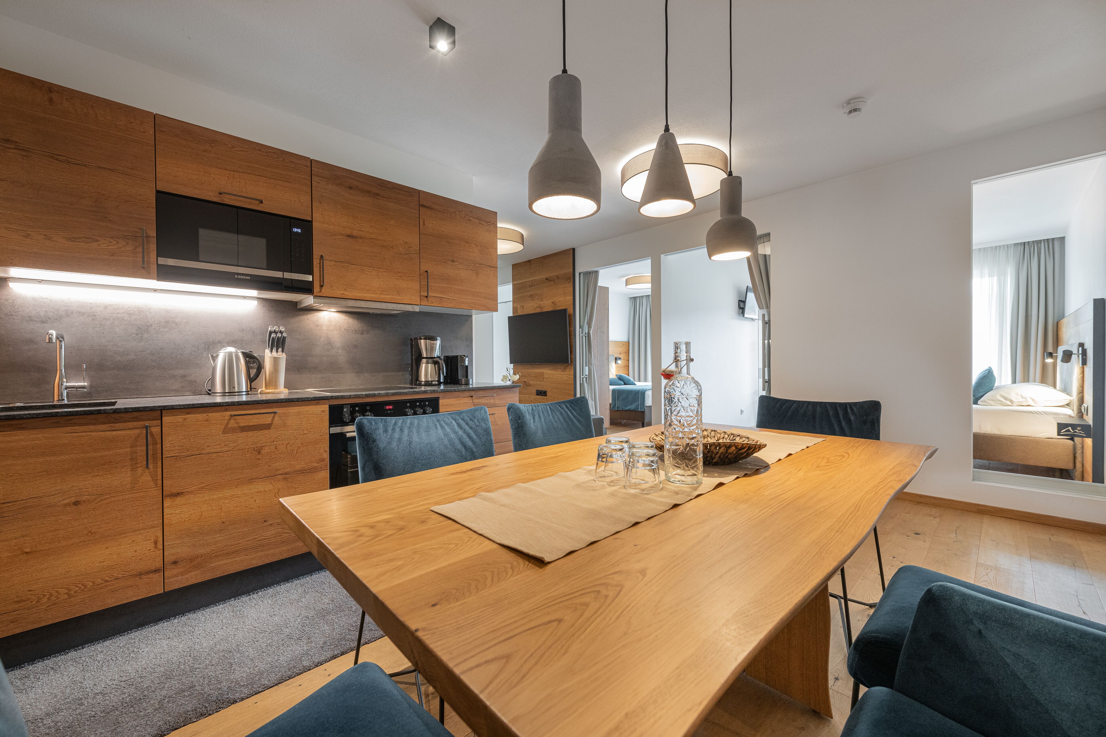 A modern kitchen with wooden cabinets, a large dining table, and pendant lighting.
