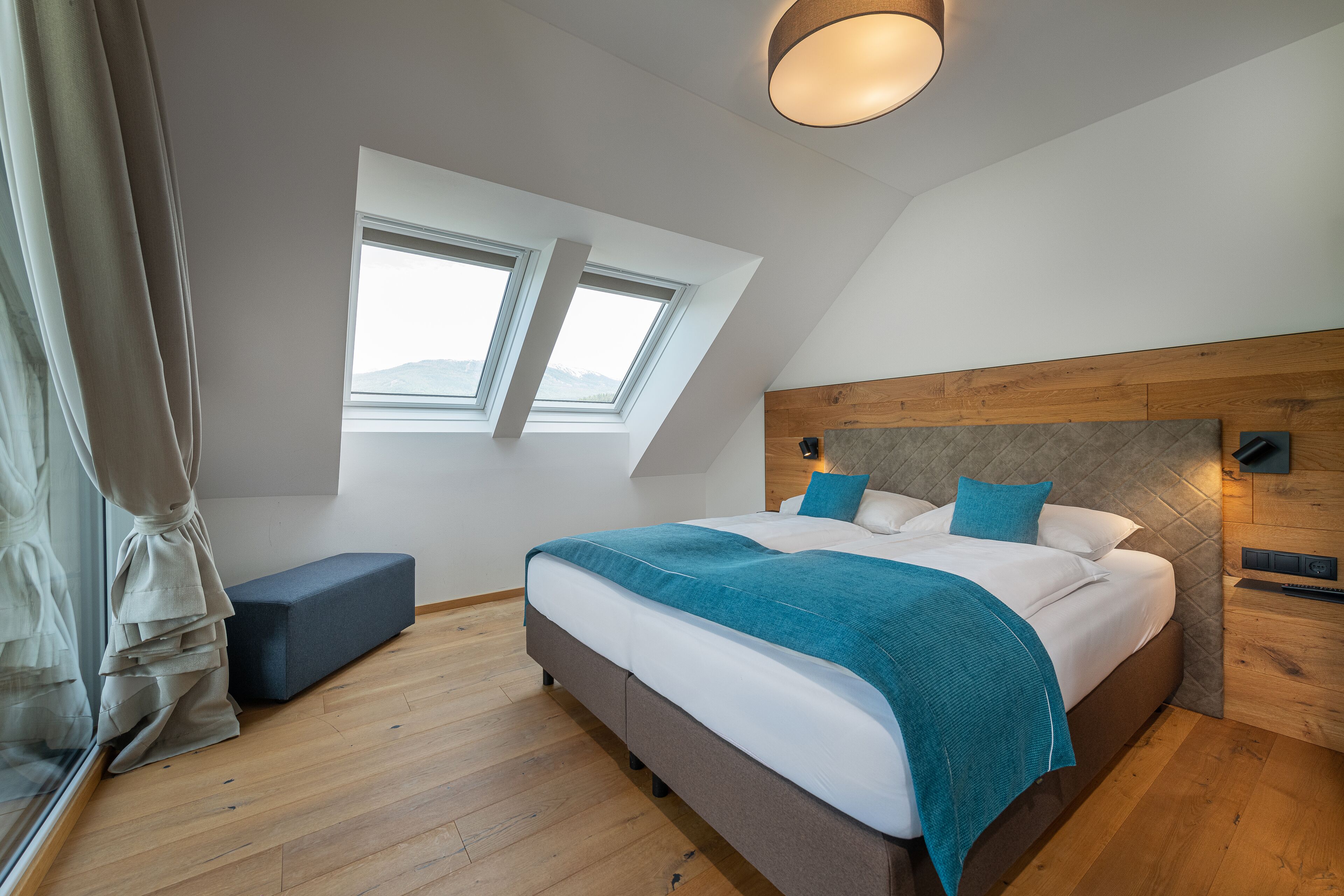 Une chambre à coucher moderne avec un grand lit, une lucarne, un banc et une tête de lit en bois.