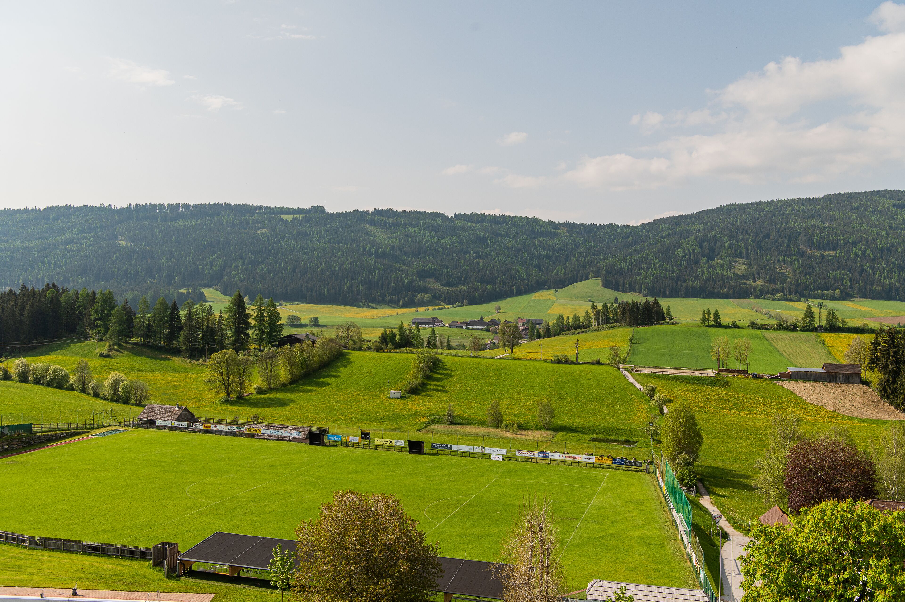 A rural landscape with green fields, a small building, and a fence.