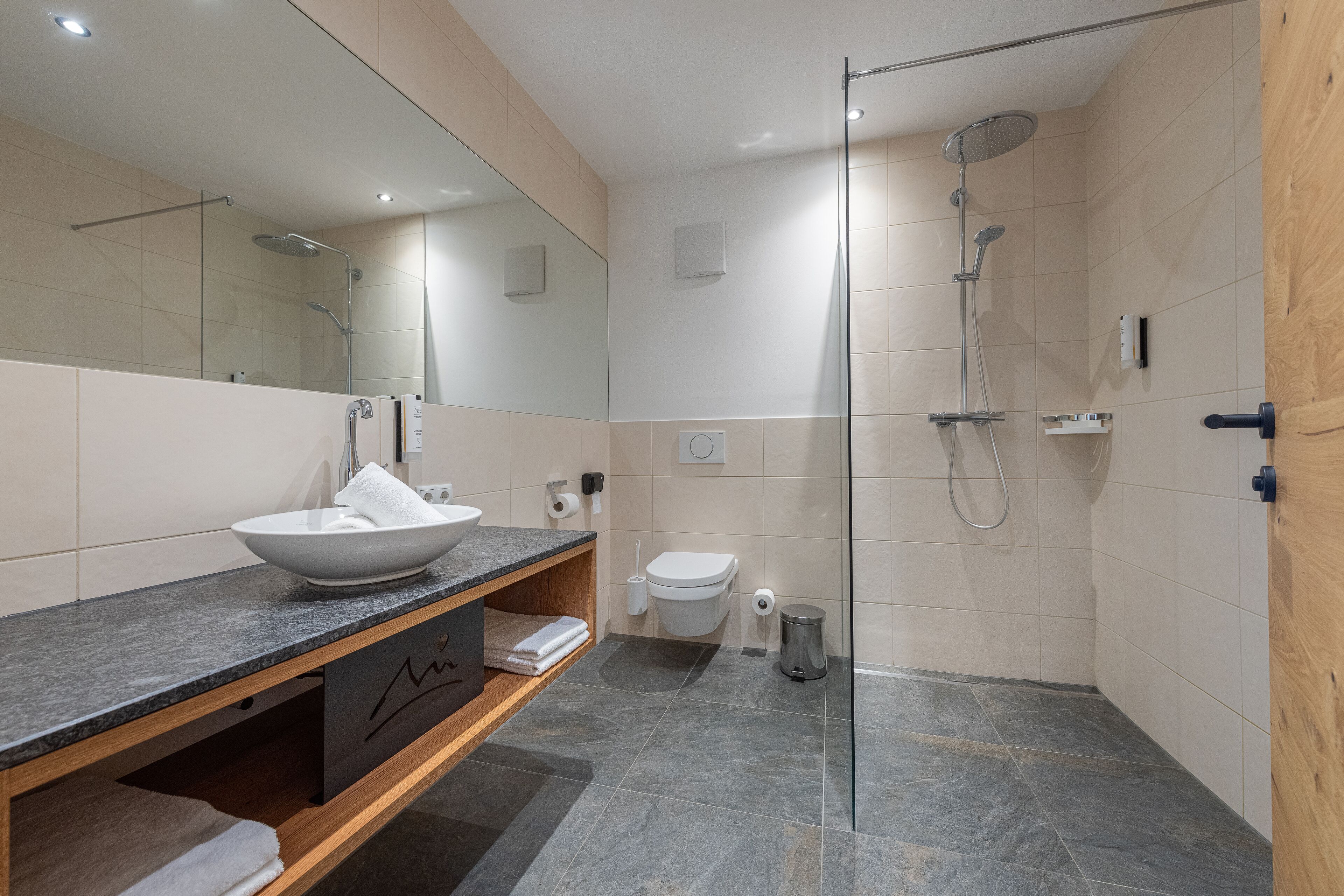 A modern bathroom with a glass-enclosed shower, a white sink, and a wooden vanity.
