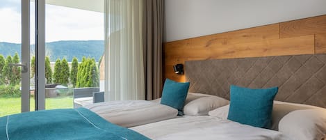 A hotel room with a large bed, a wooden headboard, and a view of greenery and mountains through the window.