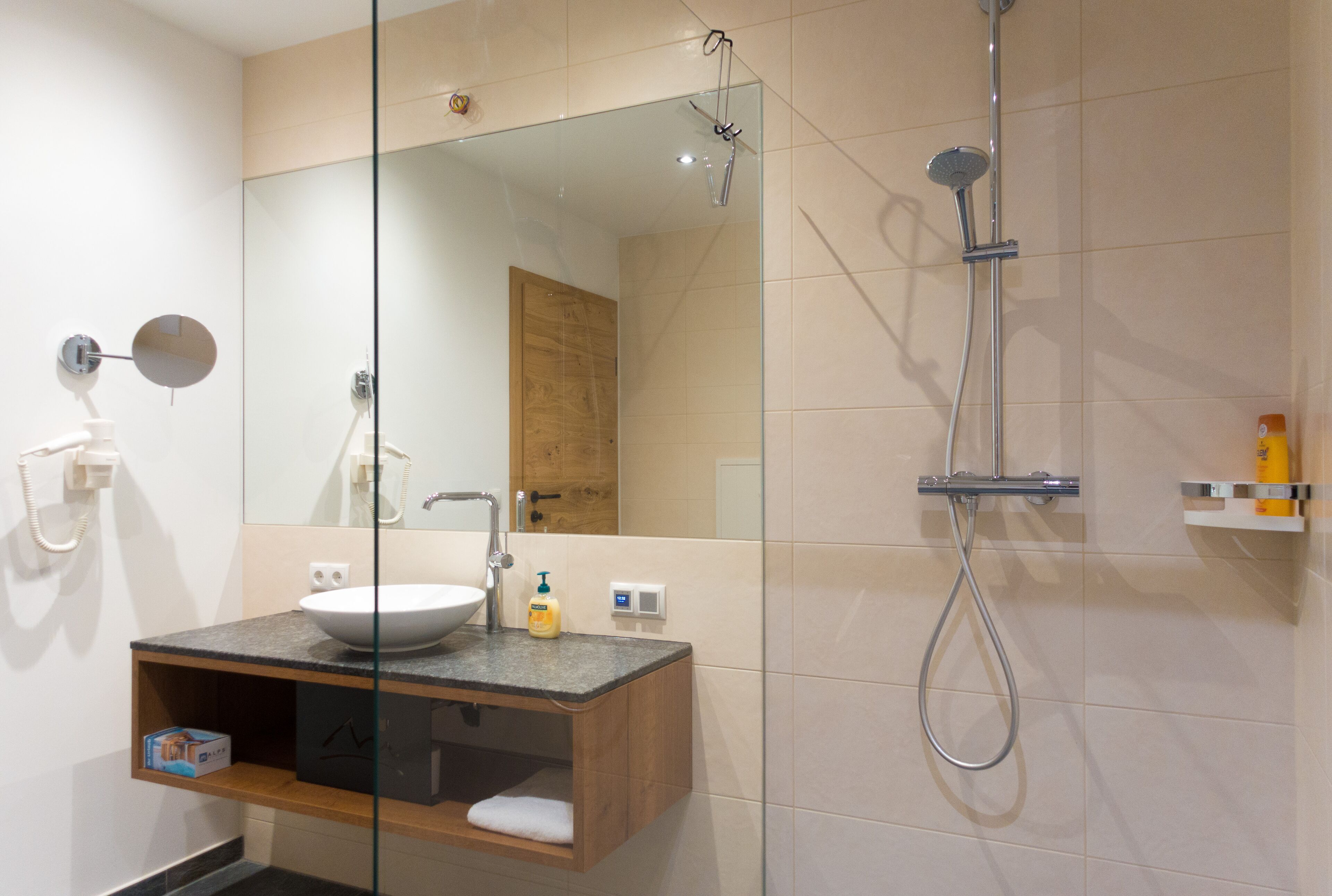 Un baño moderno con cabina de ducha de vidrio, tocador de madera y un espejo grande.