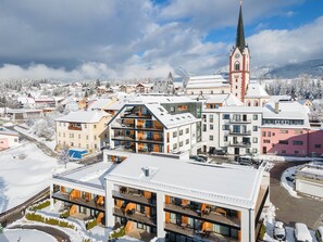 Ein modernes Hotel mit mehreren Etagen, Balkonen und Blick auf eine Kirche sowie eine verschneite Landschaft.
