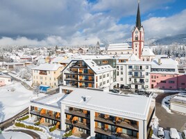 Um hotel moderno com vários andares, varandas e vista para uma igreja e paisagem coberta de neve.
